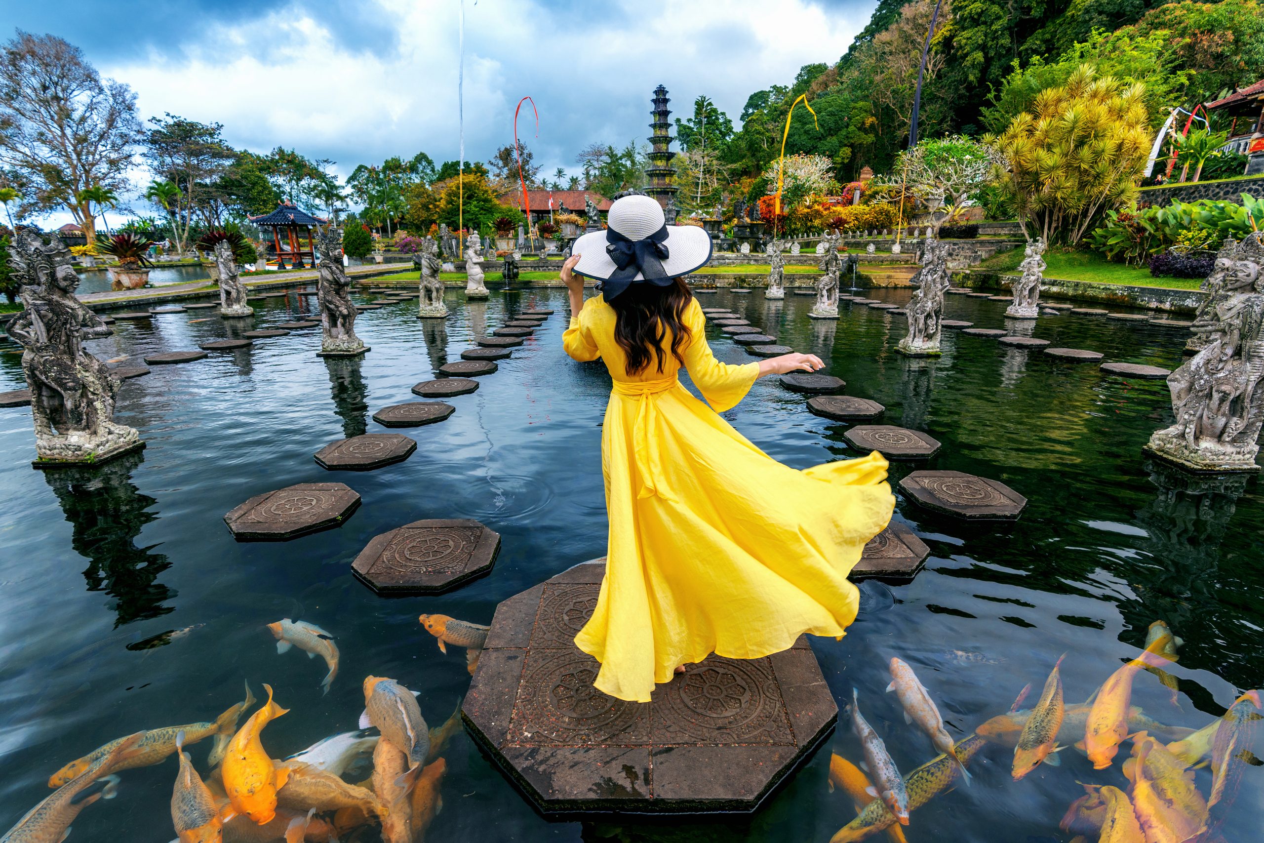 Woman standing in pond with colorful fish at Tirta Gangga Water
